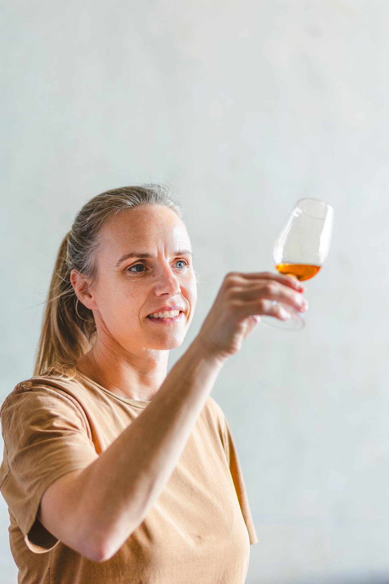 Woman holding a glass of rum and looking at it in the light.